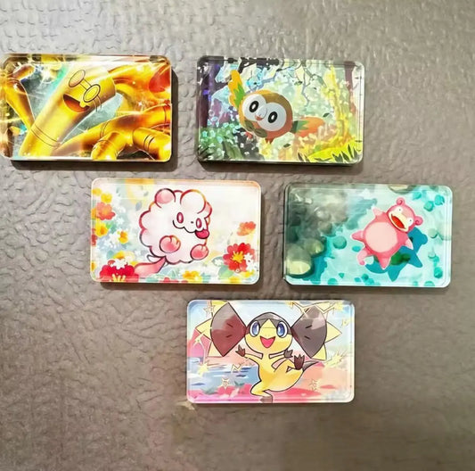 Five rectangular acrylic keychains featuring colorful cartoon Pokémon characters, arranged on a textured gray surface.